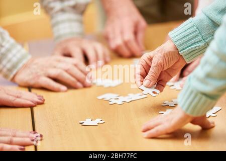 Hand of a senior citizen holds a piece of the puzzle while playing a puzzle in a retirement home