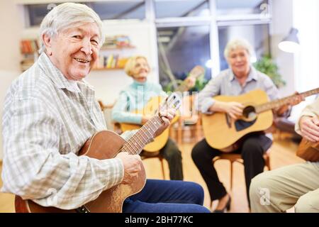 Cheerful senior man playing guitar in a guitar course at the community college Stock Photo