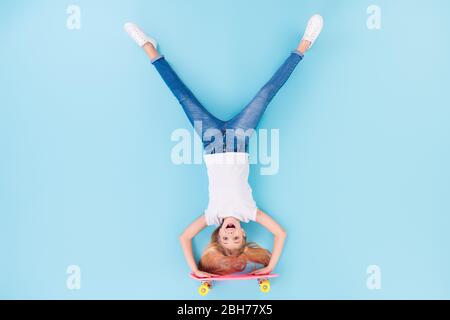 Top above high angle view full body photo of positive girl sporty kid ride longboard upside down show tongue out wear white clothes lay isolated over