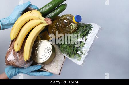 Safe Home Food Delivery. A box of different food such assortiment with hands in protective gloves. Donation, View from above Stock Photo