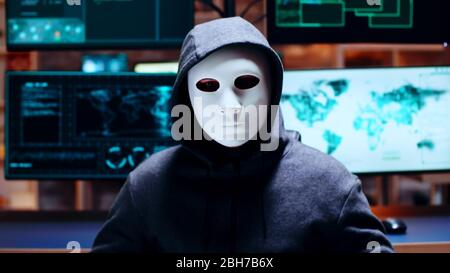 Zoom in shot cyber criminal wearing a white mask looking at the camera. Stock Photo