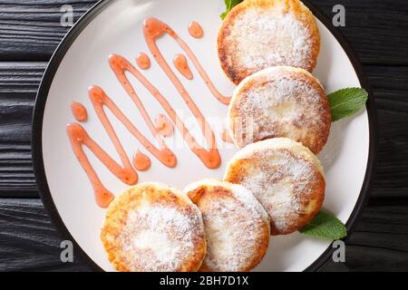 Ukrainian cuisine syrniki with powdered sugar and strawberry jam close-up in a plate on the table. horizontal top view from above Stock Photo