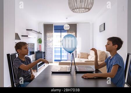 Children learning with laptop computer and play with balloon at home. Technology, education, online distance learning for kids Stock Photo
