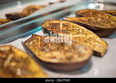 Rows of gilled aubergine halves sitting on baking paper in a stainless steel tray Stock Photo