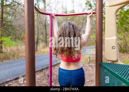 Young fit woman girl doing pull ups on bar in playground park in Virginia with sports bra back behind with long hair Stock Photo