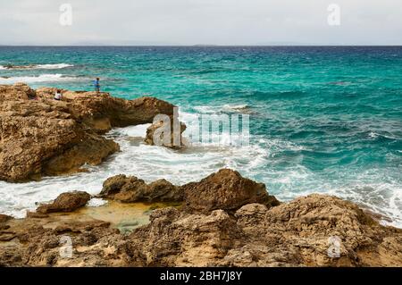 Fisherman on the rocks by Es Carnatge coastline with blue rough waters near Es Caló (Formentera, Pityuses, Balearic Islands, Mediterranean sea, Spain) Stock Photo