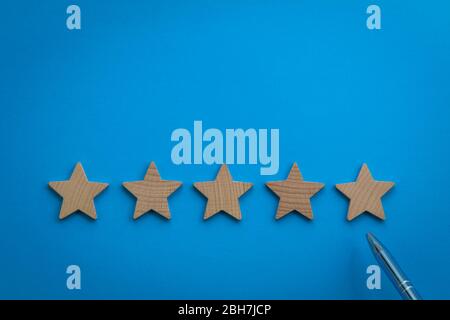 Five Star rating concept with wooden stars on blue paper background Stock Photo