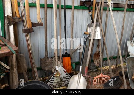 set of many different old rusty vintage gardening equipment near fence at shed storage in house backyard. Rustic agricultural home tools at barn wall Stock Photo