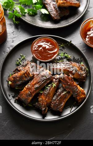Spicy hot grilled spare ribs on plate over black stone background. Tasty bbq meat. Stock Photo