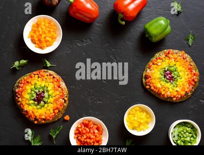 Frame of rainbow veggie bell peppers pizza and ingredients on black stone background. Vegetarian vegan or healthy food concept. Gluten free diet dish. Stock Photo