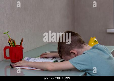 Tired sad boy studying at home online during quarantine. ired sad boy studying at home online. Fall asleep at the desk while doing homework. Stock Photo