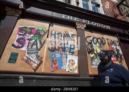 Homerton, London, UK. 24th Apr 2020. A man wearing a face mask passes the boarded up Homerton pub in East London, calling people to stay home. Due to the Covid-19 outbreak. Credit: Marcin Nowak/Alamy Live News Stock Photo