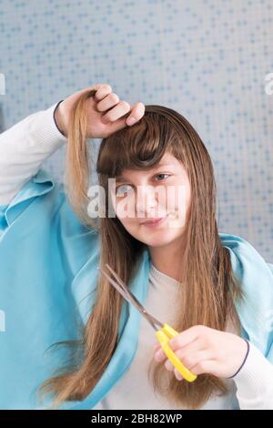 A beautiful young girl is holding a scissor to cut her hair herself during  lockdown of coronavirus, looking in mirror. DIY hair cut during the epidemi  Stock Photo - Alamy