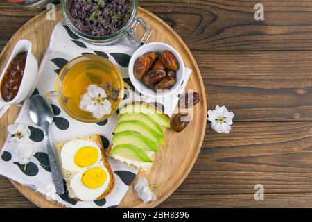 Avocado and Egg Toasts with tea and dates on the wooded board. The concept of healthy eating. Top views with clear space Stock Photo