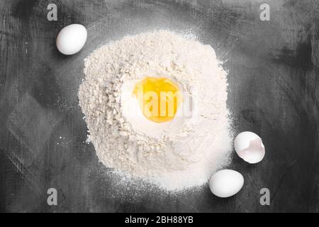 Broken raw egg in heaps of wheat flour on dark background Stock Photo