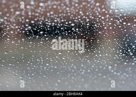 Closeup of raindrops on a windshield, blurry wipers cleaning the glass ...
