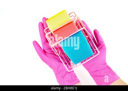 Female hands wearing pink disposable gloves hold a small shopping basket full of multicolored dish washing sponges. Top view, isolated on white. Stock Photo