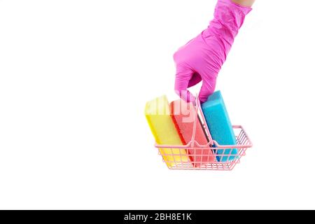Female hand in pink nitrile gloves holds a miniature shopping basket full of multicolored dishwashing sponges. Side view, isolated on white Stock Photo
