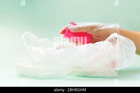 Plastic waste pink glass in a gloved hand on a blue background. Concept of plastic recycling and the environment. Selective focus. Stock Photo