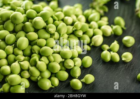 Macro close up view of fresh shelled peas on a black slate plate. Black and green contrast from healthy vegan cuisine, the freshness of the nature Stock Photo