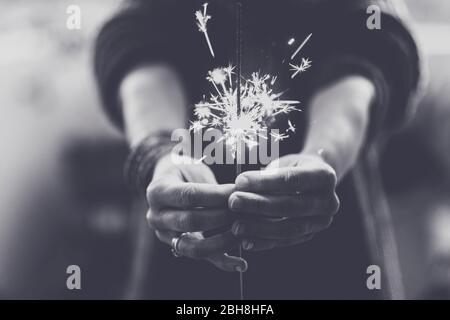 Hope and faith concept with fire light sparkler taking by woman hands and showing in front - black and white party romantic concept - close up spark light with hands - human freedom concept Stock Photo