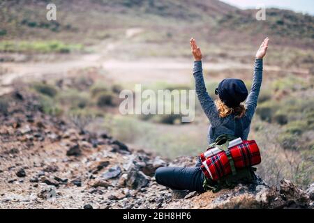 Rear view of woman with blonde curly hair doing yoga position and meditate during travel trekking hiking adventure activity - enjoying and feeling the nature - people healthy lifestyle Stock Photo