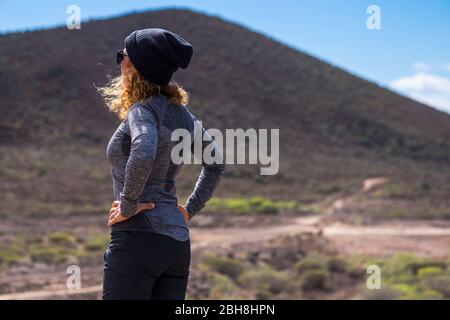 Curly woman viewed from rearoking the way and stand in the outdoor natural place- hiking equipment and sport active lifestyle for active people - trekking concept for female Stock Photo