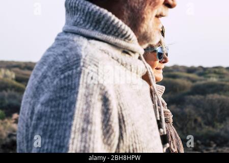 Portrait fashion style mature couple old aged seniors man and woman with nature in background - cold season autumn or spring and sun