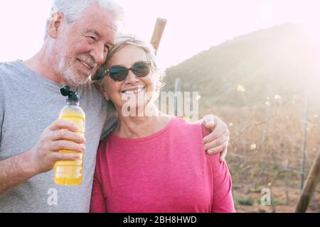 Happy cheerful aged senior couple smile and enjoy together forever life in outdoor country side with sun in backlight after a healthy fitness session Stock Photo
