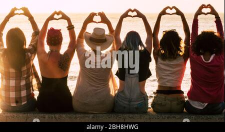 Love and meditation lifestyle concept - group of women looking at the sunset on the ocean and make the hearth with hands - romantic golden light and valentine's day concept - friendshp forever Stock Photo