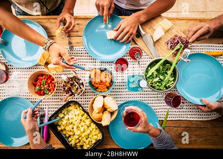 People eating together in friendship or family celebration with table full of food viewed from vertical top - friends and have fun concept - colors and background with wooden table Stock Photo