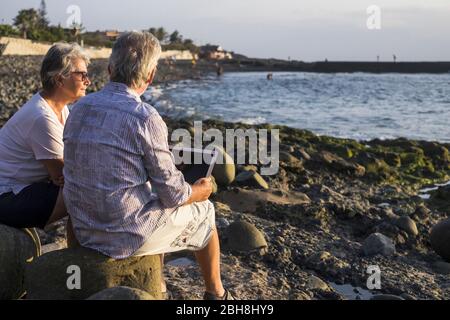 concept of vacation, technology, tourism, travel and people - happy senior couple with tablet pc computer on pebble beach with blue sea background. White hair Stock Photo
