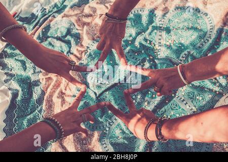 Close up with above top view of group of women hands together doing the V like victory sign - team crew work and friendship concept - blue mandala textile background on the fllor Stock Photo