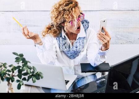 Young business woman manager shout at the phone during work call - stress and people using technology in the office at the desk - female boss shouting at mobile cellular device Stock Photo