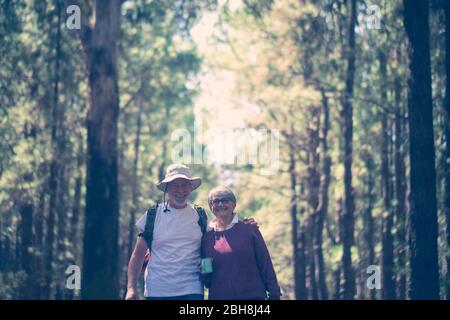 Happy caucasian senior couple smile and enjoy the travel with backpack in the outdoor nature forest - alternative free vacation concept for aged people - joyful lifestyle and hug and love Stock Photo