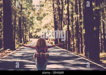 Eternity and success satisfaction life concept with lonely girl curly hai rin the middle of long road in the forest with open arms and backpack - wanderlust and travel style people Stock Photo