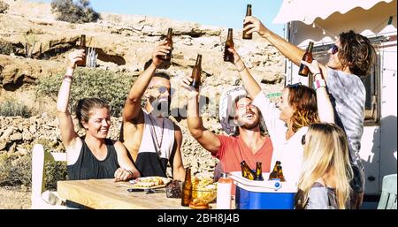 Fun success and friendship concept with group of young men and women people all together toasting with beers and food sitting on a rural wood table with nature in background Stock Photo