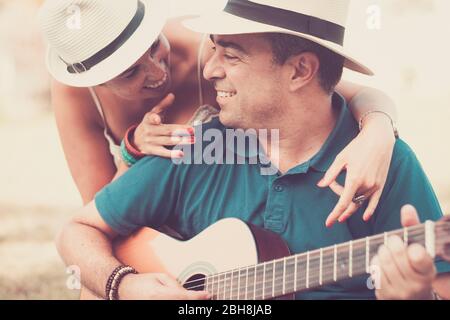 Romantic hug an colors with cheerful happy middle age people in love playing a guitar together looking and smiling - relationship for middle age adult caucasian couple - vintage filter tones Stock Photo
