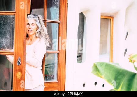 Silver society adult people caucasian woman with long white hair looking outside home from open door - alternative diversity people concept - portrait of pretty aged female Stock Photo