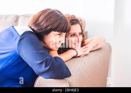couple od two women friends stay close together on the sofa smiling and