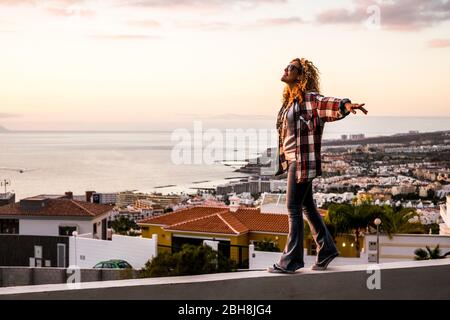 Creativity happiness freedom and craziness concept with young beautiful curly blonde woman walking in balance on a wall with city and coastline down in the background - cheerful people enjoy