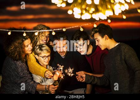 Group of friends celebrate together christmas night or new year eve or birthday or party like anniversary using sparkles light and having a lot of fun in friendship - mixed generations and families concept Stock Photo