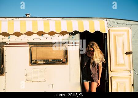 Old style american concept with beautiful blonde young girl on the door of a vintage old caravan - diversity and alternative travel style and vacation holiday adventure - freedom and tiny house Stock Photo
