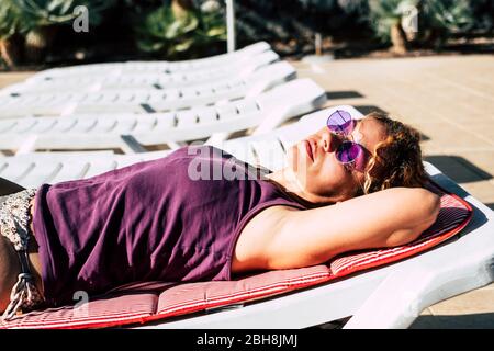 Beautiful middle age caucasian woman lat down doing sunbath in summer on sunbeds. relaxed and sleeping under the sun - vacation holiday concept - violet colors Stock Photo