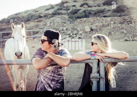 Couple of young people caucasian boy and girl inside the horse box with white beautiful animal in background - friendship and enjoy the nature outdoor concept Stock Photo
