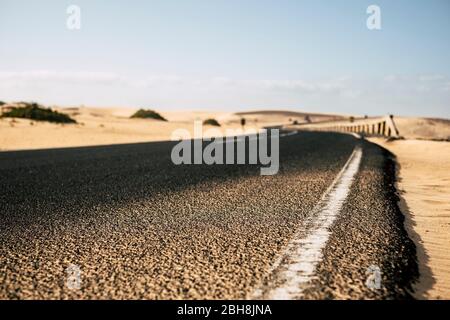 Ground close up point of view of black asphalt long road with desert sand dunes on the sides - travel and explore destination alternative summer holiday concept - focus on the first part and defocused backgorund Stock Photo