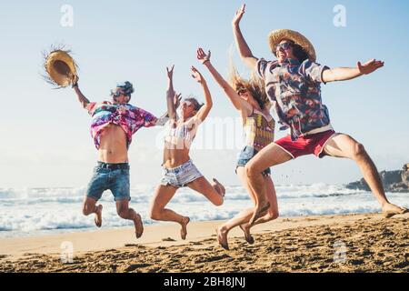Happiness and youthful generation people have fun together in friendship at the ebach for summer holiday vacation jumping like crazy and laughing a lot with blue sea and sky in background Stock Photo