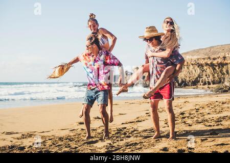Happy group of people on vaation - youthful and funny concept with young men and women having fun together in friendship playing - boys carrying girls on their back - laugh and smile Stock Photo
