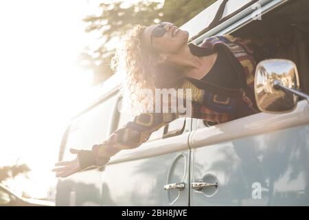 Happiness and freedom lifestyle concept with beautiful girl young caucasian female out of the vehicle enjoying the wind and feel the open air - travel and vacation transport concept for fashion girl Stock Photo