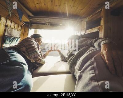 Hipster traveler adult couple enjoying the tiny van camper house lay down onthe bedroom and looking the sunset outdoor with nature - love concept for forever life together happy people Stock Photo